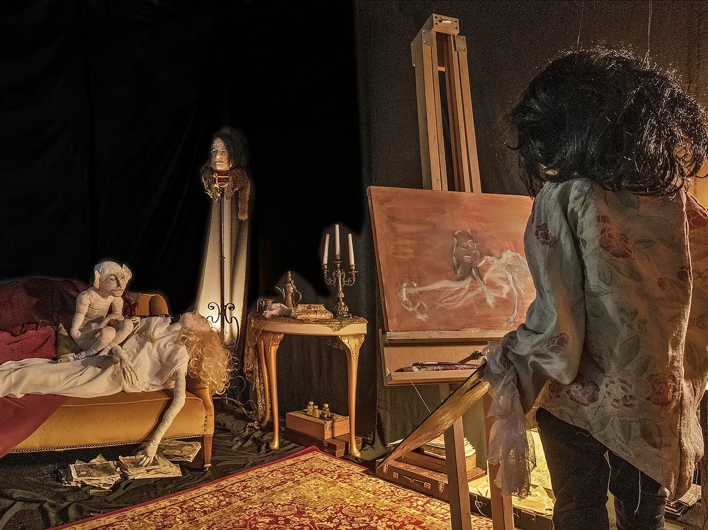 Wide view of room with painter sculpture, painting, easel, sofa, a lying woman sculpture and a leprechaun sitting on her chest.