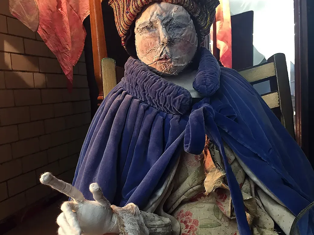 Man in background dressed in blue cloak pointing with his index finger towards attic space.