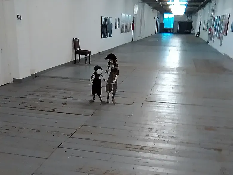 Two boys sculptures holding hands are walking along an industrial corridor.