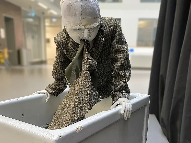 Boy wearing a tweed jacket is vomitting torn fabric strips into sink.