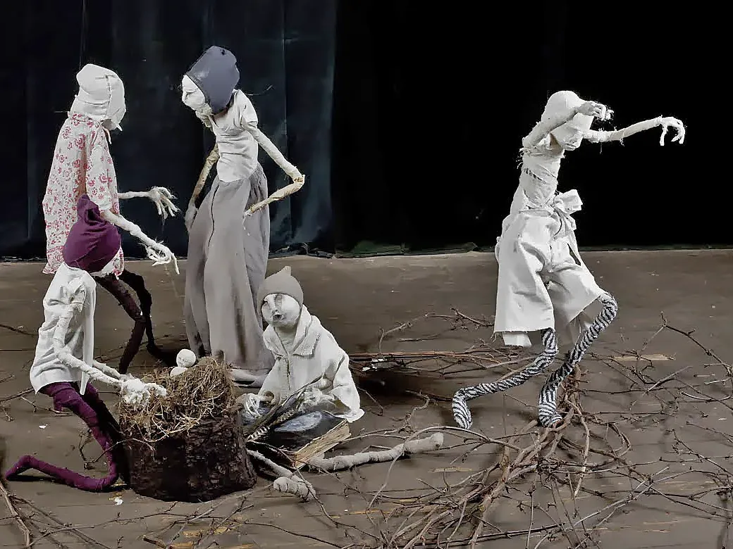 Five boy sculptures on a stage either chatting, reading or dancing. A basket with straw and an infant in the center.