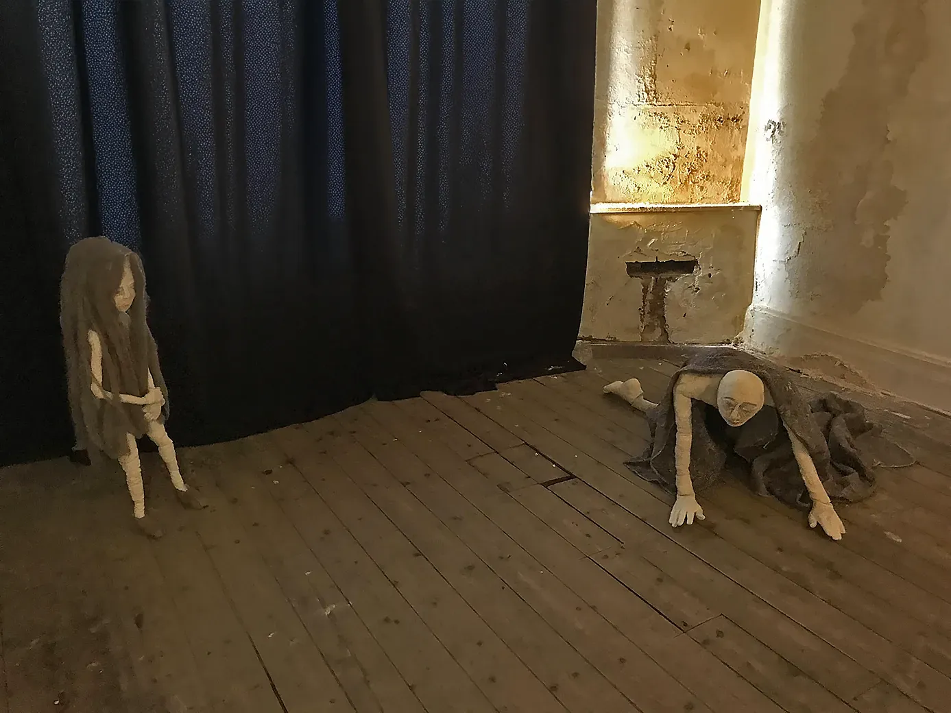 Two female sculptures 3 metres apart. A girl standing up with long woolly hair, the other a woman who crawls on the floor with a woollen blanket over her back.