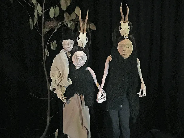 Male and female sculptures with a child in prehistoric clothes in front of dark leafy background.