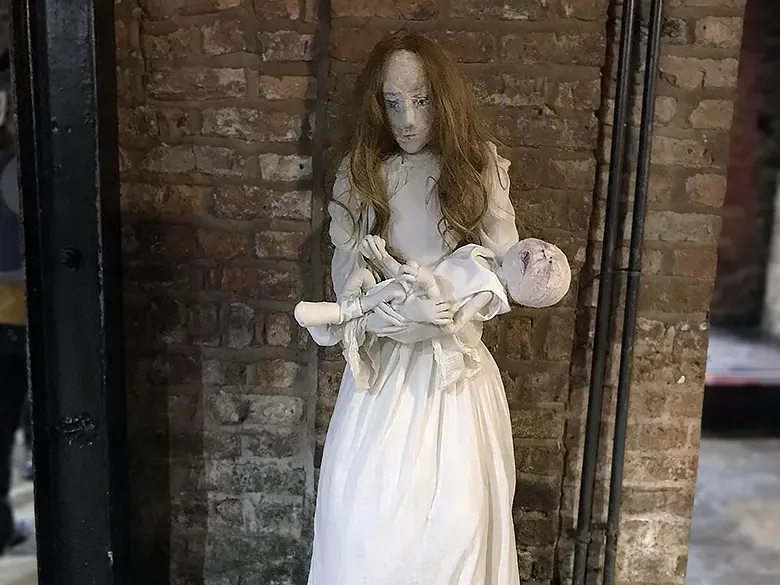A girl sculpture holding a baby in front of a stone wall.