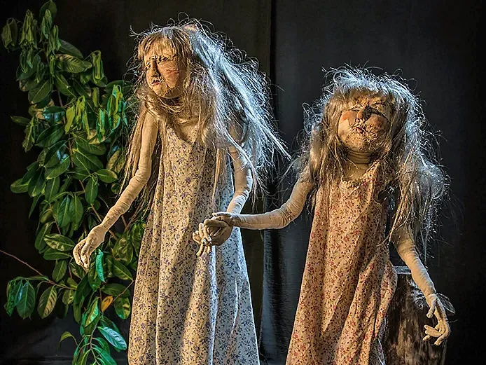 Two girl sculptures walking through a dark garden.