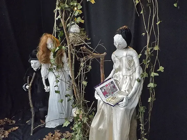 Staging of two girl sculptures and one boy within branches and leafs.