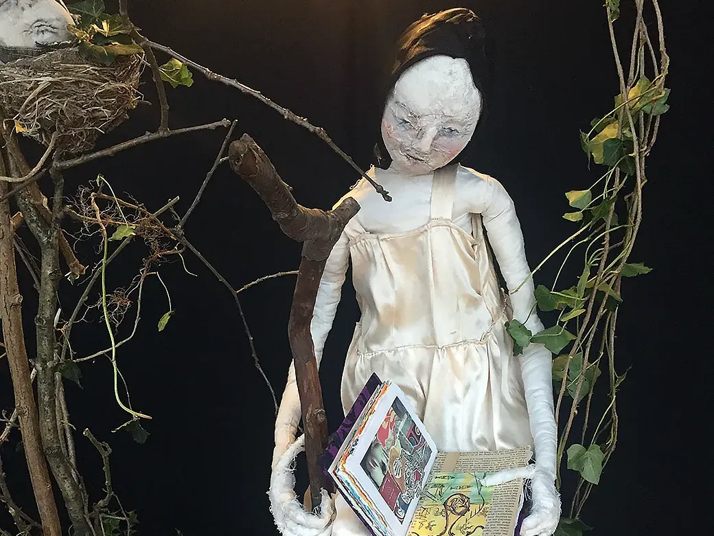 Girl sitting on branch holding an open book.