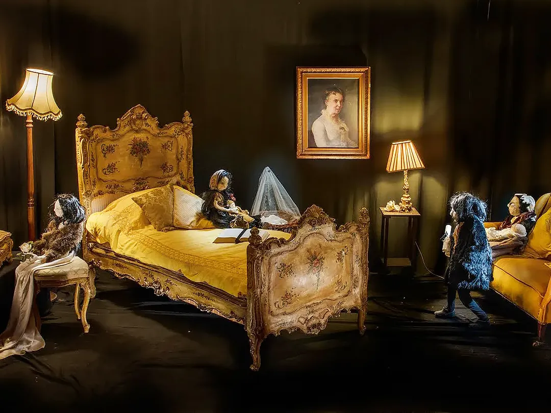 Wide view of a room installation with seven human-like sculptures and antique furniture.