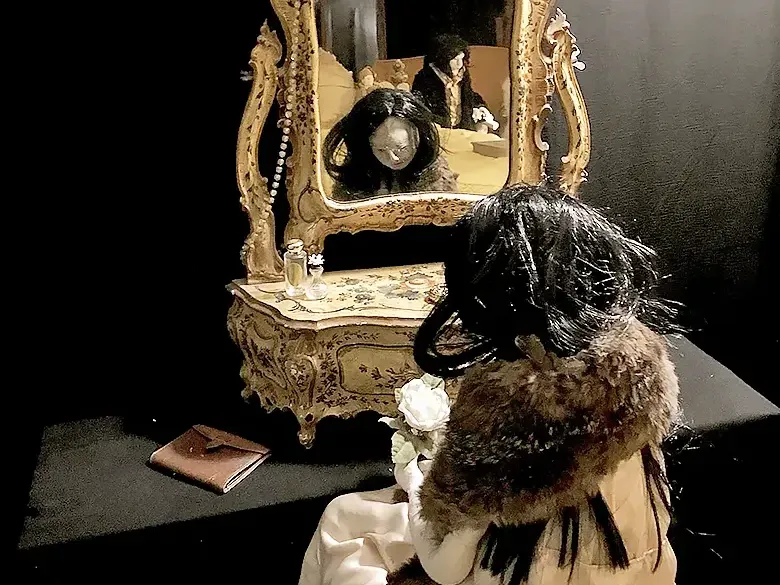 Woman figure sitting at antique dressing table looking into mirror.