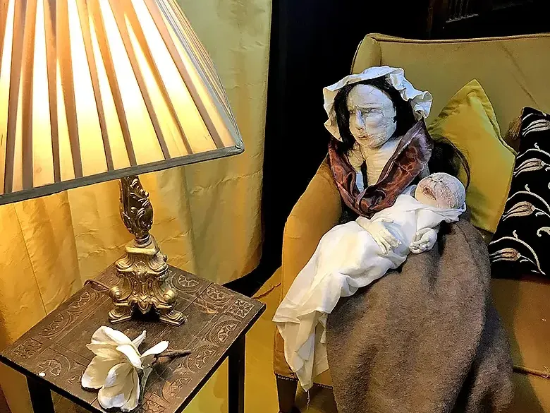 Side table with a lamb and sofa with a woman figure holding a baby.